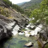 Un río cristalino serpentea entre rocas pulidas en la Garganta de los Infiernos. Dos personas disfrutan del agua fresca en este paisaje natural.