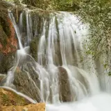 Cascadas de Hueznar, un velo de agua blanca desciende por rocas cubiertas de musgo y vegetación exuberante.