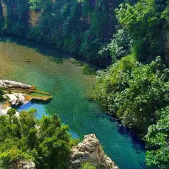 Un río de aguas cristalinas serpentea entre acantilados cubiertos de vegetación exuberante. Los lagos de Anna, un paraíso natural de tonos turquesa y verdes intensos.