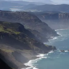 Majestuosos acantilados de San Andrés de Teixido se alzan sobre el mar Cantábrico, con verdes laderas y el azul profundo del océano.