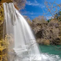 Cascada de agua blanca cayendo sobre rocas ocres, como los ojos del Cabriel, en un día azul.