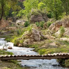 Un puente rústico cruza un arroyo en un paisaje rocoso y verde. Descubre cómo llegar a este rincón natural.