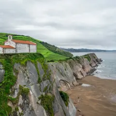 Iglesia blanca con tejado naranja sobre acantilado verde, junto al mar Cantábrico. Un lugar que evoca la esencia de "8 apellidos vascos".
