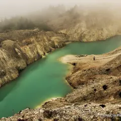 Laguna turquesa en el monte Neme Carballo, rodeada de tierra y rocas, con niebla al fondo.