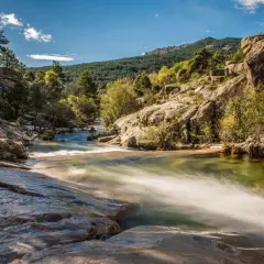 Un río serpentea entre rocas y vegetación, un paisaje idílico para descubrir rutas con encanto cerca de Madrid.