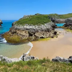 Una cala escondida entre acantilados verdes, con aguas turquesas y arena dorada. Un rincón idílico entre las mejores playas de Asturias.