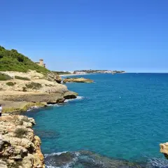 Dos personas caminan por el camí de ronda de Tarragona, disfrutando de las vistas al mar azul y la costa rocosa.