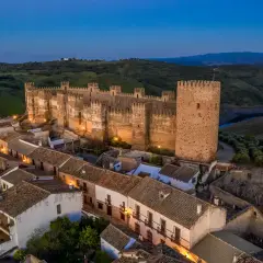 Imponente castillo, posiblemente el castillo más antiguo de España, iluminado al anochecer sobre un pueblo blanco.