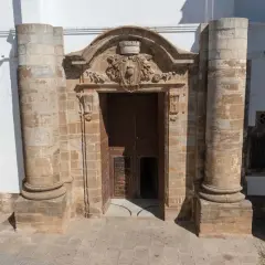 Impresionante portal de piedra con detalles ornamentales, flanqueado por columnas. Parece la entrada a una capilla Sixtina extremeña, invitando a descubrir su interior.