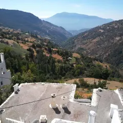 Paisaje montañoso con casas blancas y tejados planos. El camino a Trevélez se abre paso entre verdes colinas y valles profundos bajo un cielo azul.