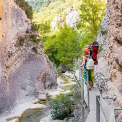 Senderistas disfrutan de las **pasarelas del Vero**, un camino metálico que serpentea por un cañón rocoso con un río cristalino.