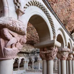 Detalles arquitectónicos y escultóricos en piedra de San Juan de la Peña, con arcos y capiteles tallados bajo una roca.