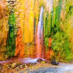 La cascada de los colores, un espectáculo natural con agua cayendo sobre rocas teñidas de vibrantes tonos ocres, verdes y amarillos.