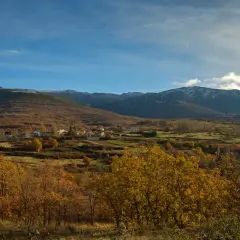 Paisaje otoñal con un pueblo en la ladera. Las montañas nevadas al fondo sugieren la ruta a la laguna negra.