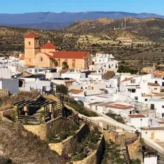 Vista panorámica de Lucainena de las Torres, un pueblo blanco andaluz con una iglesia de campanario naranja. El camino para llegar serpentea entre colinas áridas.