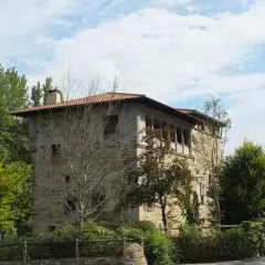 Edificio de piedra con tejado rojo y balcones, rodeado de árboles verdes. Un lugar con encanto, ideal para saber artziniega como llegar.