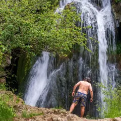 Hombre de espaldas admira la cascada en la ruta del barranco de la Hoz. Naturaleza exuberante y agua en movimiento.