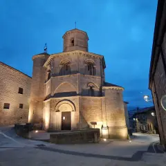 Las torres del río iluminadas al anochecer, con una iglesia románica y calles empedradas.