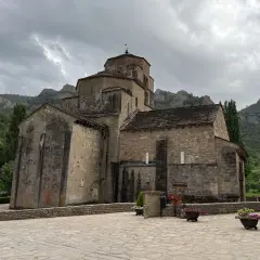 Iglesia románica de piedra con montañas al fondo. Un lugar histórico que evoca la grandeza del puente la reina.