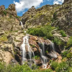 La cascada de los litueros desciende por rocas escarpadas, rodeada de vegetación exuberante bajo un cielo azul con nubes.