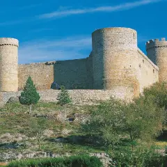 El castillo de Cornago se alza imponente sobre una colina, con sus torres circulares y murallas de piedra bajo un cielo azul intenso.