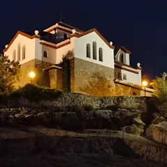 La ermita de los Tres Juanes, iluminada de noche, se alza sobre una colina rocosa.