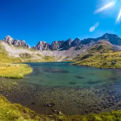 El ibón de Acherito, un lago de montaña de aguas cristalinas, rodeado de prados verdes y picos rocosos bajo un cielo azul intenso.