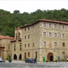 Edificio de piedra con tejados rojos, parte del monasterio de Santo Toribio de Liébana, rodeado de vegetación.