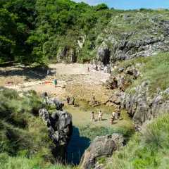Gente disfrutando del sol y el agua cristalina en la playa de cobijero, rodeada de rocas y vegetación exuberante.