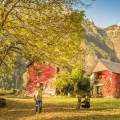 Dos mujeres y un perro disfrutan del otoño en el valle de Pineta, ideal para rutas. Las casas cubiertas de hiedra roja y las montañas crean un paisaje idílico.