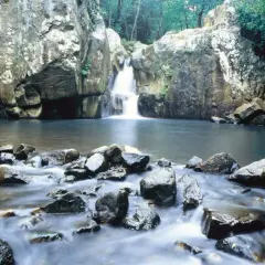 Cascada y río en la ruta del Río de la Miel, rodeado de rocas y vegetación exuberante.