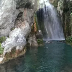 Cascada en las fuentes del Algar, con aguas turquesas y vegetación exuberante entre rocas.