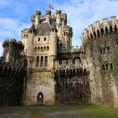 El imponente castillo de Butrón, con sus torres y murallas de piedra, se alza majestuoso bajo un cielo azul con nubes.