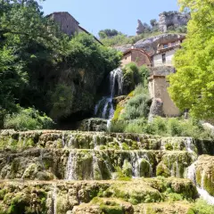 Cascada en las Hoces del Ebro, con casas de piedra integradas en la roca y vegetación exuberante.