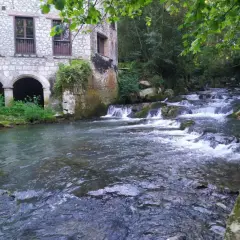 Edificio de piedra con arcos junto a un río con cascadas. Parece la fuente del francés, un lugar idílico.