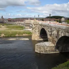Puente romano en Hospital de Órbigo, con arcos de piedra y andamios. Al fondo, el pueblo y un hostal.