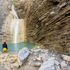 Un grupo de barranquistas se prepara para descender una cascada de oros bajo, rodeados de imponentes paredes rocosas estratificadas y una poza de agua turquesa.