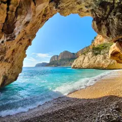 Vista desde una cueva en Cala Moraig, con aguas turquesas y acantilados dorados bajo un cielo azul.