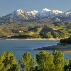 El pantano de los Bermejales, con montañas nevadas al fondo y colinas verdes salpicadas de olivos.