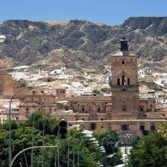 Vista panorámica de Guadix, con su imponente torre campanario y casas blancas al pie de montañas rocosas. Ideal para planificar cómo llegar.
