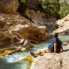 Hombre sentado junto a un río turquesa en un cañón rocoso. Un lugar idílico para explorar, ¡así es como llegar!