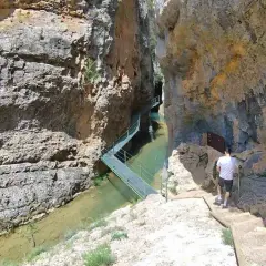 Un hombre camina por las pasarelas de Calomarde, un sendero metálico que serpentea sobre un río entre imponentes paredes rocosas.