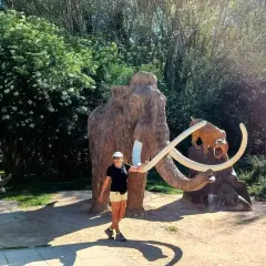 Una mujer sonríe junto a un mamut y un tigre dientes de sable, parte de la ruta del mamut. Un rinoceronte se ve a la izquierda.