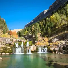 Cascada en un valle montañoso con árboles otoñales, ideal para las mejores rutas senderismo España.