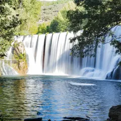 El Salto del Pelgo, una cascada imponente con agua sedosa cayendo sobre rocas, rodeada de vegetación exuberante y un estanque azul profundo.
