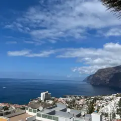 Vista panorámica de acantilados imponentes y el mar azul, con un pueblo costero y un puerto deportivo. Un lugar que evoca las mejores playas de Tenerife.