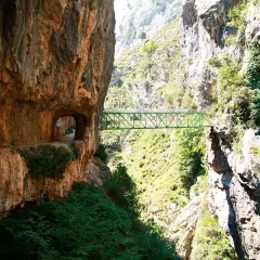 Un puente verde cruza un desfiladero rocoso, parte de la ruta del Cares. El tiempo parece perfecto para esta aventura.