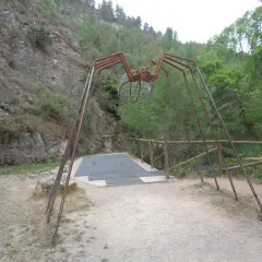 Escultura de araña gigante en la ruta de las esculturas Bogarra, con un cuerpo de alambre y patas metálicas, sobre un camino de grava.