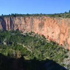 Impresionante cañón con paredes rojizas y vegetación verde. Los puentes colgantes de Chulilla se asoman entre la naturaleza.