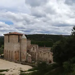 Ruinas del monasterio de San Pedro de Arlanza, con su torre robusta y arcos de piedra bajo un cielo nublado.